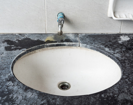 Dirty basin with the stained metal faucet in the public toilet of the urban park.の写真素材