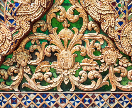 Sculptured wood with the golden paint in the traditional Thai style on the triangle gable of the Thai church.の写真素材