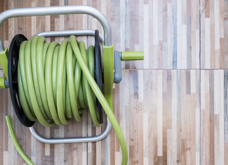 Green rubber hose of the plastic reel set on the wooden pattern tile for use in the home garden.の写真素材