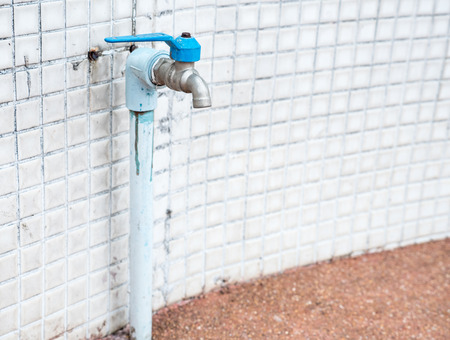 Blue faucet with the dirty pipe near the tile wall of the urban house.(Select focus)の写真素材