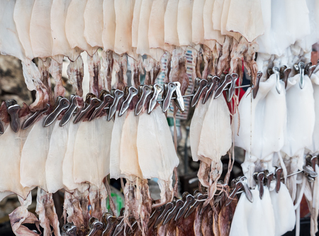 Fresh and dry squid is hanging on the wire row for sale to the traveler in the local market of the...