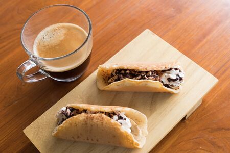 Banoffee pancake roll and the espresso cup on the wooden table for the breakfast.