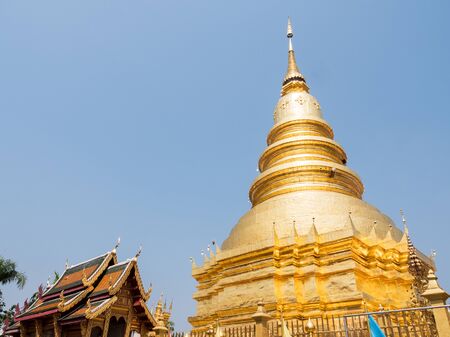The large golden pagoda in the traditional northern Thai style which near the beautiful church of the Thai temple.の写真素材
