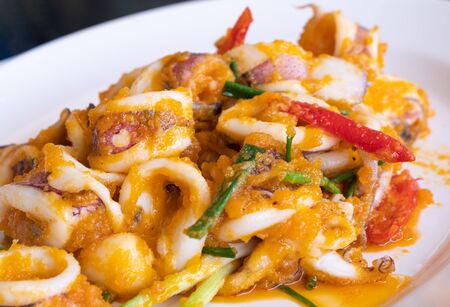 Stir fried squid with salted eggs in the white plate for dinner in the seafood restaurant.