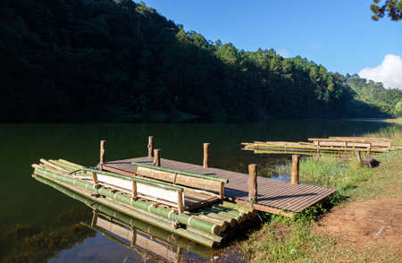The bamboo raft is floating near the wooden pier for the tourists in the tranquility reservoir of...