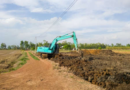 Excavator is working on earthwork for digging the ponds near the paddy field, storge the water for...