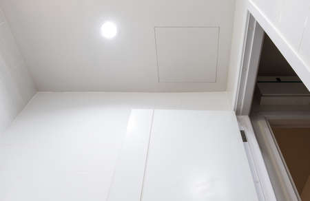 The access door on the white ceiling in the bathroom for maintenance of the electric system under the roof of the city house, above views for the copy space.の写真素材