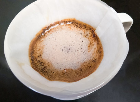 The closeup of the arabica ground coffee in the process of brewing from pouring hot water in the ceramic dripper, crema is floating over the coffee layer, front view for the background.の写真素材