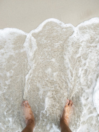 The barefoot on the beach with the white foam from the wave, relaxing in the holiday time, above view with the copy space.の写真素材