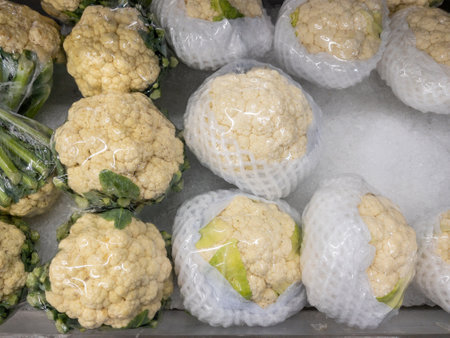 The fresh cauliflower with plastic wrap are rowing in the tray with the crushed ice for sale in the supermarket, front view with the copy space.の写真素材