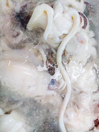 A close-up image of fresh octopus tentacles displayed on ice at a seafood market. The tentacles are submerged in water with ice cubes, highlighting their freshness and texture.の写真素材