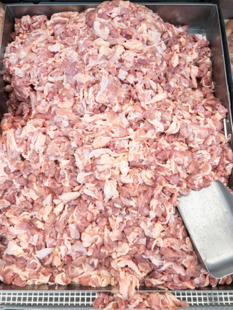 Raw chicken thigh scraps piled in a metal tray at a supermarket, fresh and ready for purchase,...