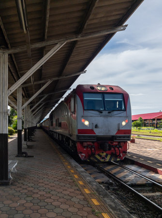 A diesel electric locomotive of the express train stops at the railway station platform under the roof, waiting to pick up passengers on a bright sunny day.の写真素材