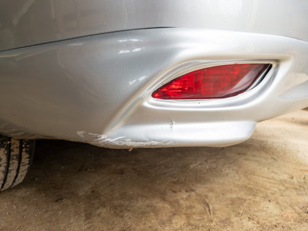 Close up of the silver car rear bumper with deep scratches and paint damage from hitting a curb,...