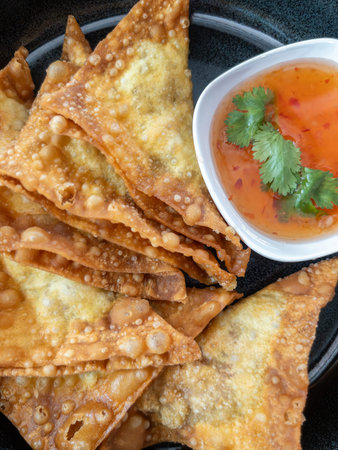 Delicious deep fried pork wontons served with sweet chili sauce and coriander on a black plate. Authentic Asian crispy pork dumpling appetizer.の写真素材