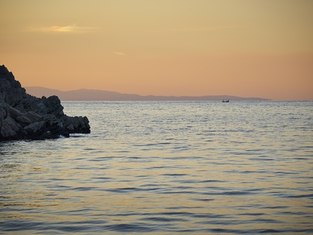 Sea, rock and distant fishermen at sunsetの写真素材