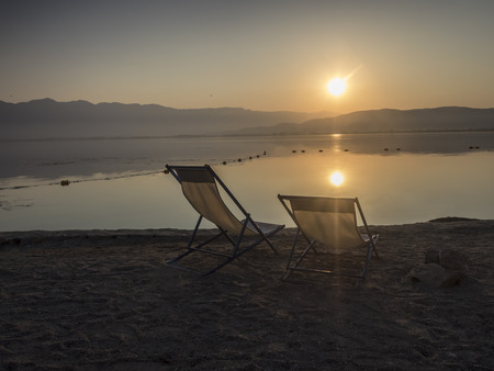 two chairs on the beach on sunrise with flareの写真素材