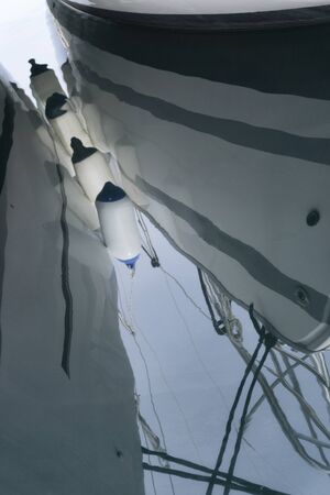 Reflection in sea of boat fenders on the side of a two sailboatsの写真素材