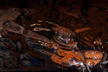 Opened Computer hard disk drive in studio with bubbles and dark red and blue reflection, conceptual...