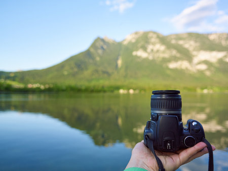 A man is holding a branded DSLR camera with one hand and wants to take a photo of the mountainsの写真素材