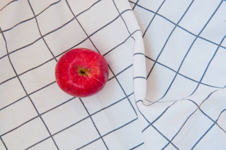Beautiful red apple on the white folded towel with square lines on the background. Concept of autumn harvest and healthy lifestyleの写真素材