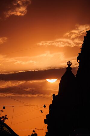 Orange cloudy sky with a part of big sun hidden behind the cloud. Sunset in the city with dark...