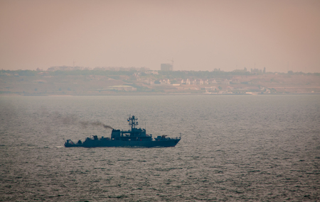 Military ship sailing in the Black sea. A shore with houses is seen at the background. Cloudy foggy weatherの写真素材