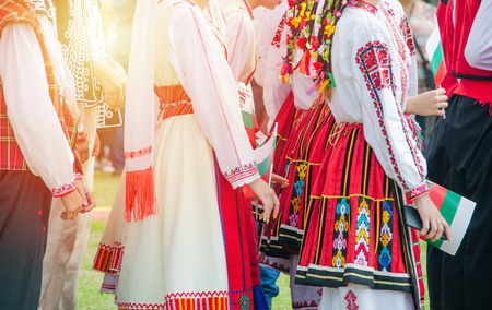 Unrecognizable irls in ethnic Bulgarian costumes with colorful ornament. Sunset at the background