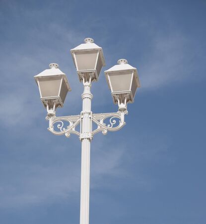Ornate white lamppost with three lamps against a blue skyの写真素材