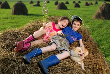 Summer lanscape with hay cocks, couple children sitting on large hayの写真素材