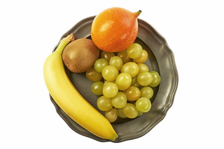 Bunch of green grapes, granadilla, kiwi and banana on a metal plate, centrally from above on a white backgroundの写真素材