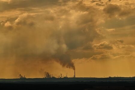 Factory in the distance, black smoke from the chimneys connects with clouds in the skyの写真素材