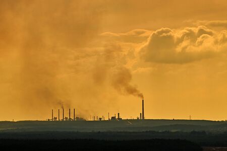 Factory in the distance, black smoke from the chimneys connects with clouds in the sky