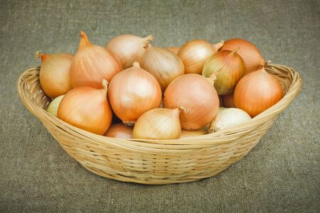 Onions in a Woven Straw Basket on a Sacking backgroundの写真素材