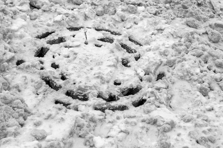 manhole sewage hatch of rain gutter ditches filled with snow after a snowstorm clogged with winter ice in black and whiteの写真素材