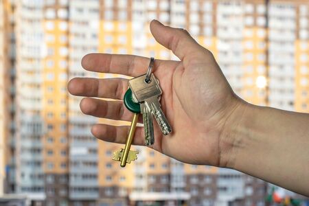 hand with the keys to a brand new apartment on the background of a multi-storey residential building houseの写真素材