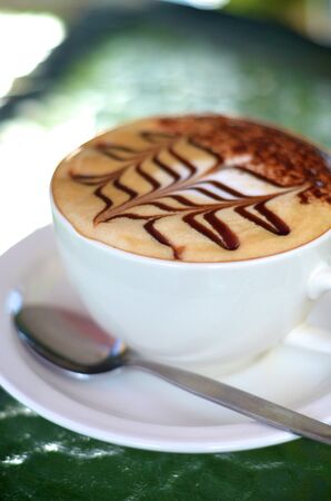 Side view of cappuccino coffee cup with spoon on glass table の写真素材