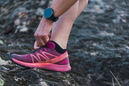 Caucasian young woman tying her shoes before trail running in the mountain. One shoe close up....