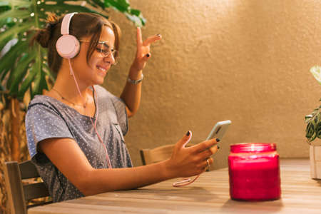 Caucasian teen girl smiling and dancing while listening to music on her smartphone. Horizontal. With...