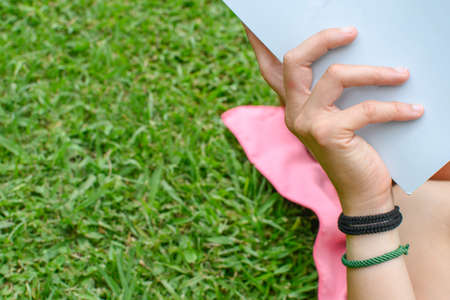 Close up of a hand holding a book lying in the grass. Horizontal. With copy space.