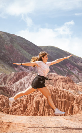 Caucasian woman jumping in a split position and open arms in the middle of a mountain road. Vertical. With copyspace.の写真素材