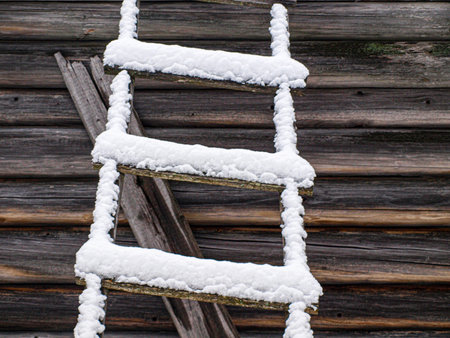 Wooden ladder covered with snow on the background of a wooden wallの写真素材
