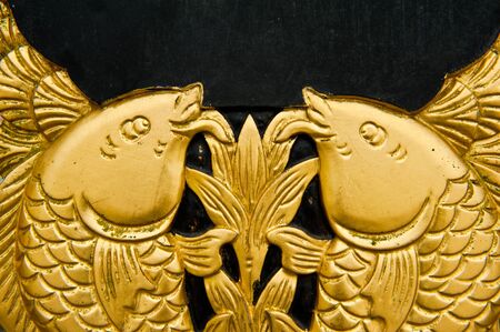 Twin golden fish sculpture on black backgroundの写真素材