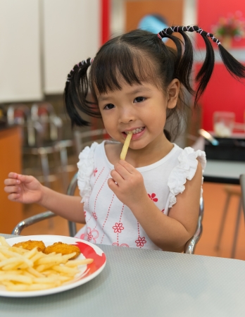 Little girl eating french fries at fast food restaurantの写真素材