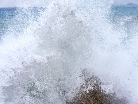 Closeup with foamy effect of a wave hitting rocks on the coast of Baunei
