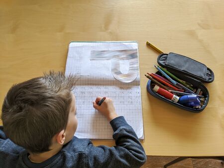 Portrait of diligent little child writing carefully sitting at desk and doing homework