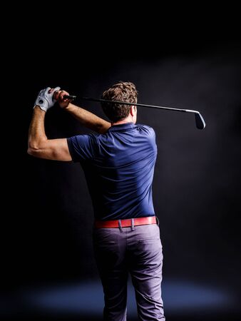 Close-up of a golf player intent on perfecting the swing isolated on dark backgroundの写真素材