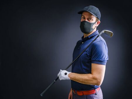 Golfer with protective mask waits for his turn to make his best shot, isolated on dark backgroundの写真素材