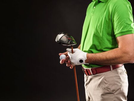 Closeup of a male golfer holding a golf ball, a golf iron and wearing a white golf glove. Horizontal format over a black background.の写真素材