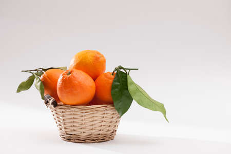 A wicker basket full of fresh orange fruits, isolated on a white background. Citrus fruit and healthy food concept.の写真素材